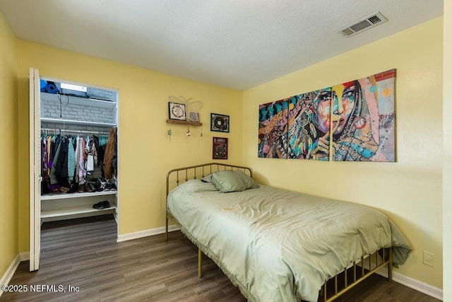 bedroom with wood finished floors, visible vents, baseboards, a closet, and a walk in closet