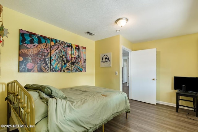 bedroom with baseboards, a textured ceiling, visible vents, and wood finished floors