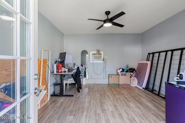 office space featuring a ceiling fan, arched walkways, a wall mounted AC, and wood finished floors