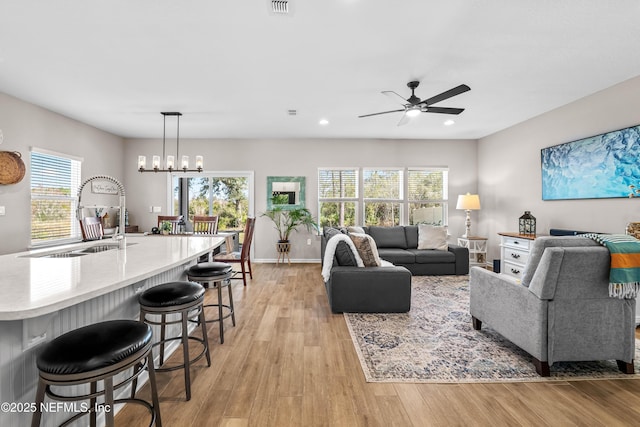 living area with recessed lighting, visible vents, light wood-style floors, baseboards, and ceiling fan with notable chandelier