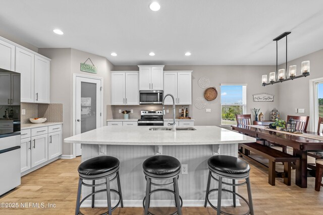 kitchen featuring a breakfast bar area, stainless steel appliances, light countertops, light wood-style floors, and a sink