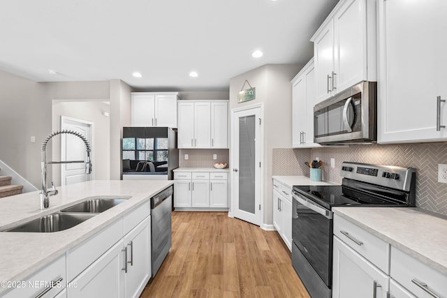 kitchen with appliances with stainless steel finishes, light countertops, a sink, and white cabinetry