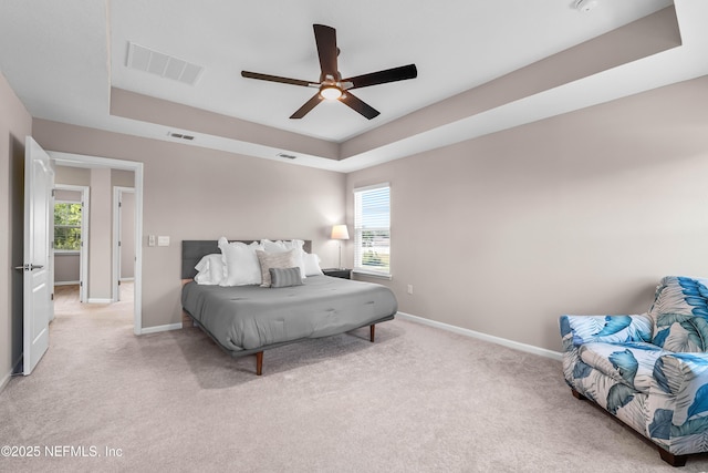 bedroom with baseboards, a tray ceiling, visible vents, and light colored carpet