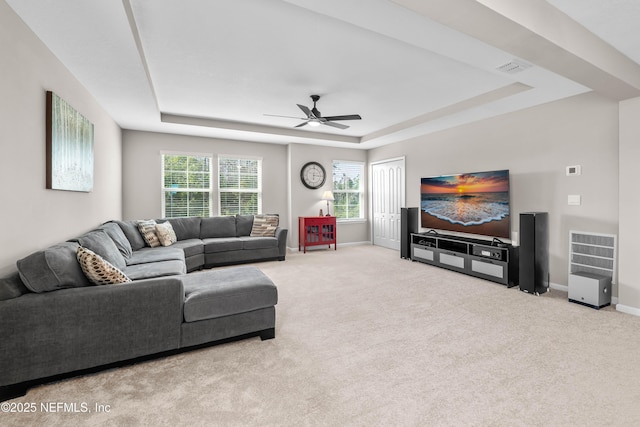 carpeted living area with baseboards, a tray ceiling, and ceiling fan