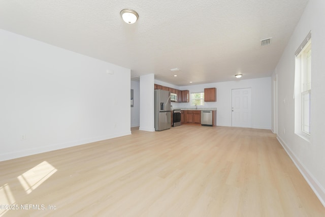 unfurnished living room with a textured ceiling, light wood finished floors, visible vents, and baseboards