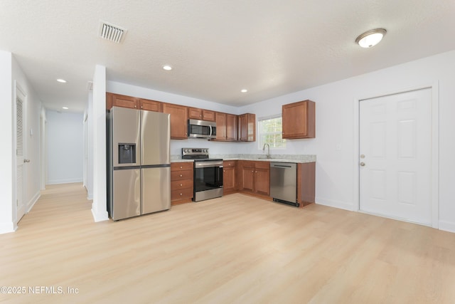 kitchen featuring visible vents, stainless steel appliances, light countertops, light wood-type flooring, and a sink