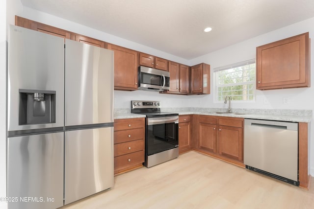 kitchen featuring brown cabinetry, stainless steel appliances, light wood-type flooring, a sink, and recessed lighting