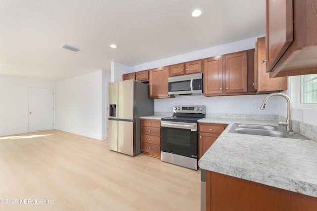 kitchen with stainless steel appliances, light countertops, visible vents, brown cabinetry, and a sink