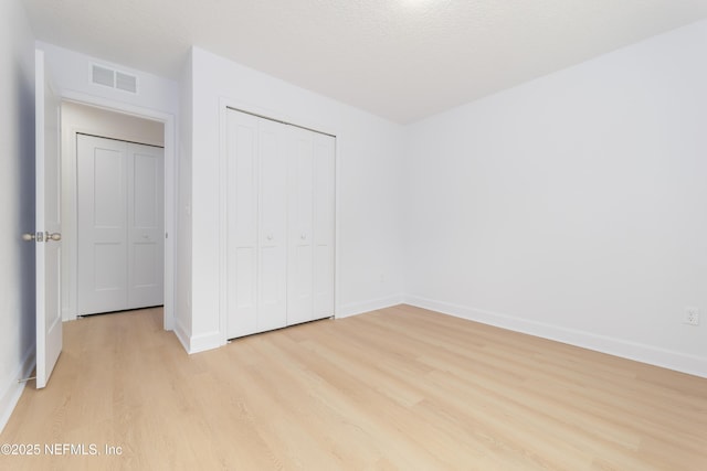 unfurnished bedroom with light wood-type flooring, baseboards, visible vents, and a closet