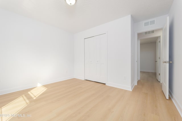 unfurnished bedroom featuring light wood-type flooring, baseboards, visible vents, and a closet