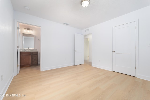 unfurnished bedroom featuring visible vents, baseboards, light wood-style flooring, ensuite bathroom, and a sink