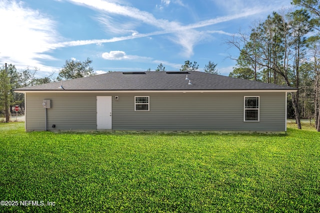 rear view of property with a shingled roof and a lawn