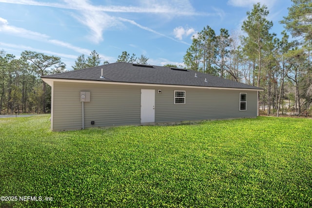 rear view of property with a shingled roof and a lawn