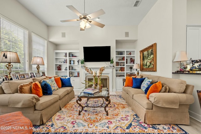 living area featuring visible vents, built in features, a fireplace, wood finished floors, and a ceiling fan