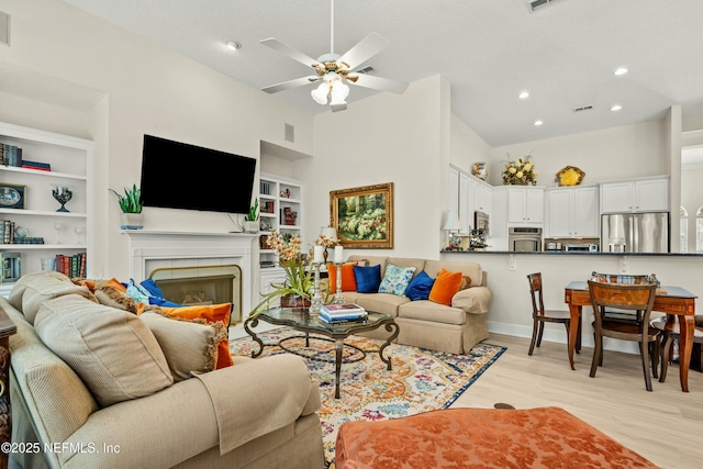 living area with visible vents, light wood-style flooring, built in features, a fireplace, and ceiling fan