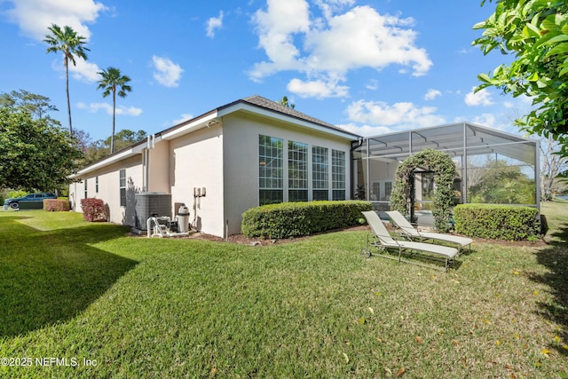 rear view of property with glass enclosure, a lawn, central AC, and stucco siding