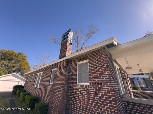 view of side of home featuring a garage, an outbuilding, brick siding, and a chimney