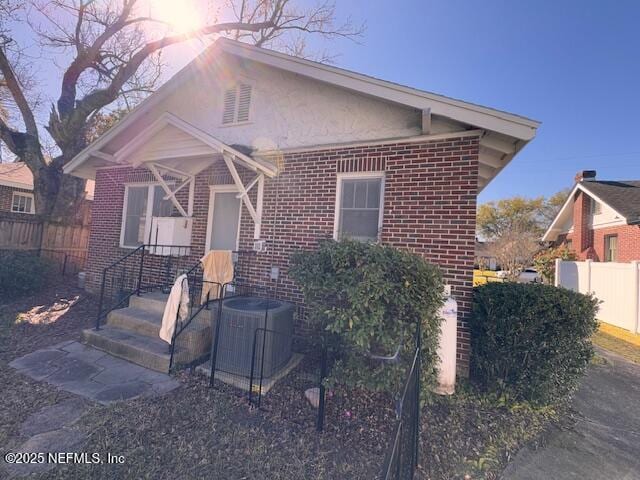 bungalow-style house with cooling unit, brick siding, and fence