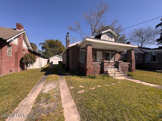 view of front of home with an outbuilding, a porch, brick siding, driveway, and a front lawn