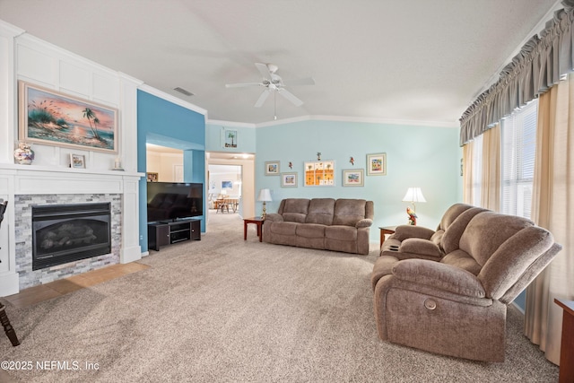 carpeted living area with a ceiling fan, visible vents, vaulted ceiling, a glass covered fireplace, and crown molding