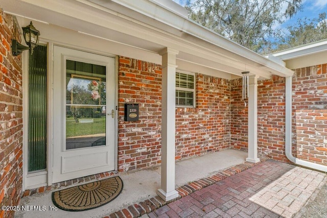 doorway to property with a porch and brick siding