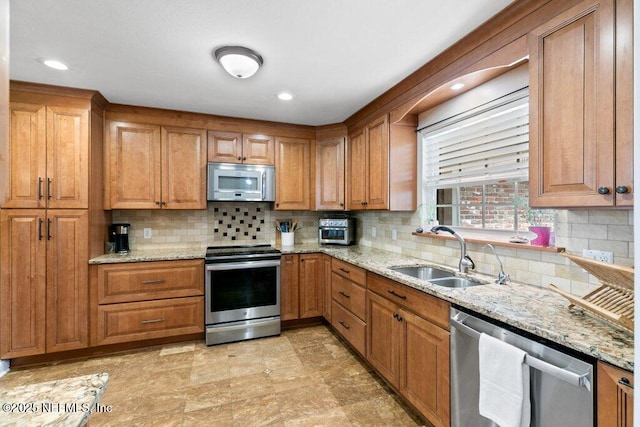 kitchen with appliances with stainless steel finishes, a sink, light stone counters, and tasteful backsplash