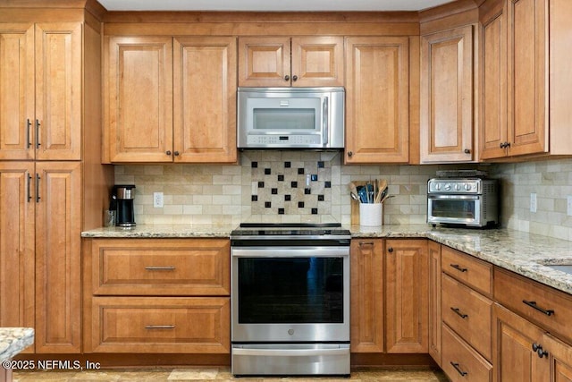 kitchen with stainless steel appliances, light stone counters, brown cabinets, and decorative backsplash