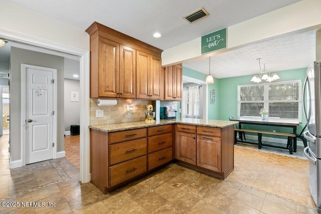 kitchen featuring brown cabinets, visible vents, decorative backsplash, freestanding refrigerator, and light stone countertops