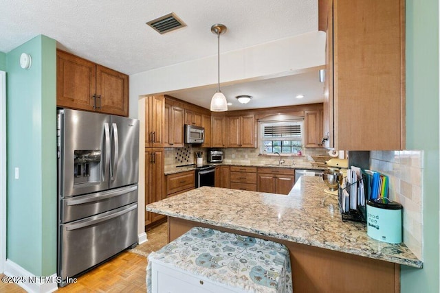 kitchen featuring brown cabinets, stainless steel appliances, tasteful backsplash, visible vents, and a peninsula