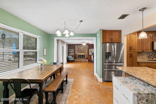 kitchen with a textured ceiling, a fireplace, stainless steel fridge, and brown cabinets