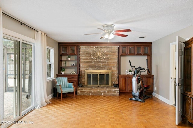 living area with a textured ceiling, ceiling fan, a fireplace, and baseboards