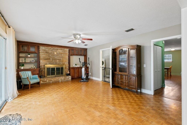 unfurnished living room featuring visible vents, a glass covered fireplace, ceiling fan, a textured ceiling, and baseboards