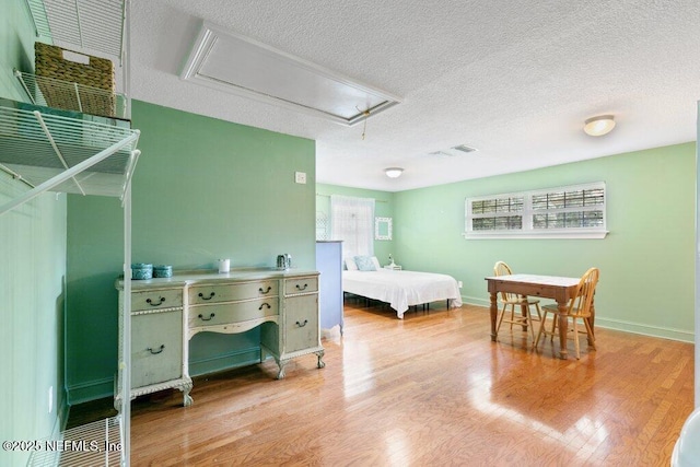 bedroom featuring a textured ceiling, light wood-type flooring, visible vents, and attic access