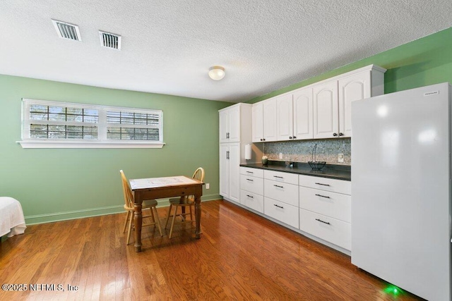 kitchen featuring visible vents, freestanding refrigerator, tasteful backsplash, dark countertops, and dark wood finished floors