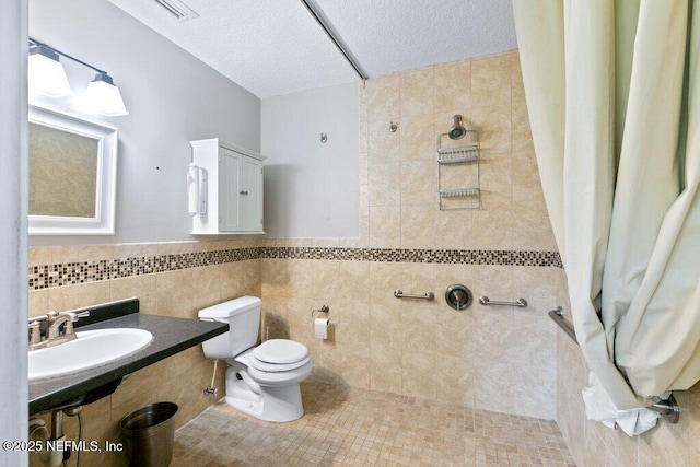 full bath with toilet, a sink, a tile shower, a textured ceiling, and tile walls