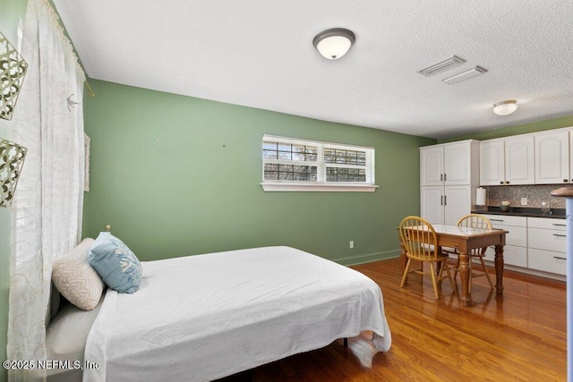 bedroom with visible vents, a textured ceiling, baseboards, and wood finished floors