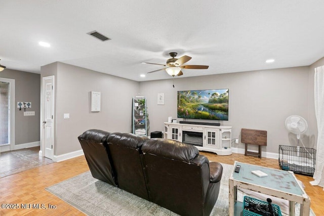 living room featuring baseboards, a fireplace, visible vents, and ceiling fan