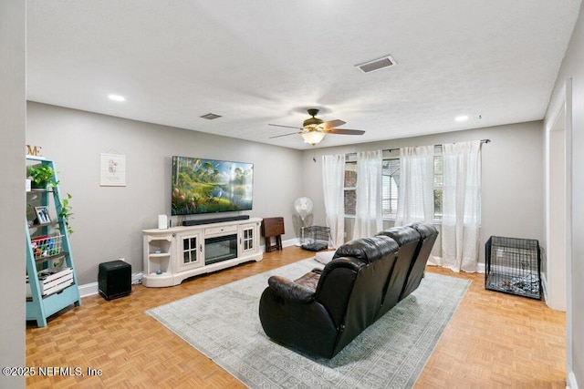 living room featuring baseboards, visible vents, ceiling fan, and a textured ceiling