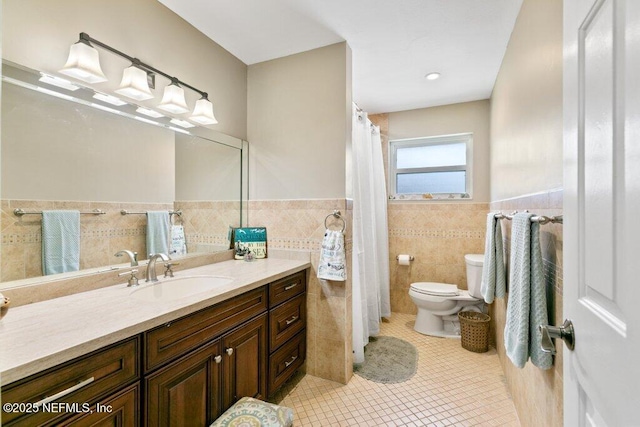 bathroom with toilet, a wainscoted wall, tile patterned floors, vanity, and tile walls