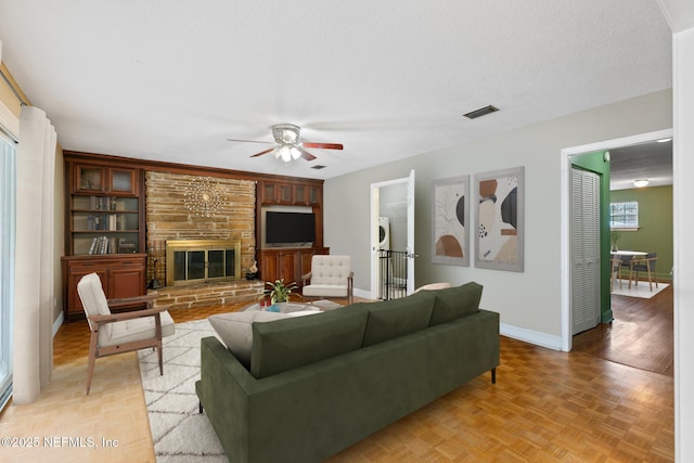 living room featuring baseboards, visible vents, ceiling fan, a textured ceiling, and a stone fireplace