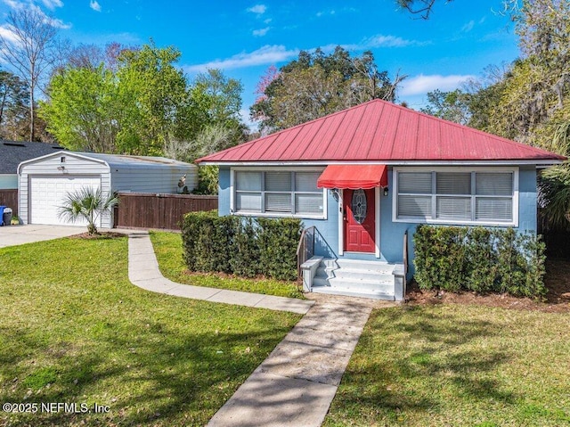 view of front of property with an outbuilding, a detached garage, metal roof, fence, and a front lawn