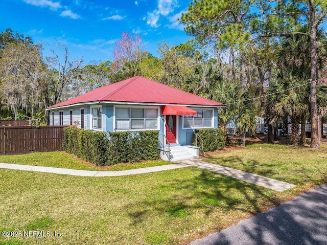 view of front of house featuring metal roof, fence, and a front lawn