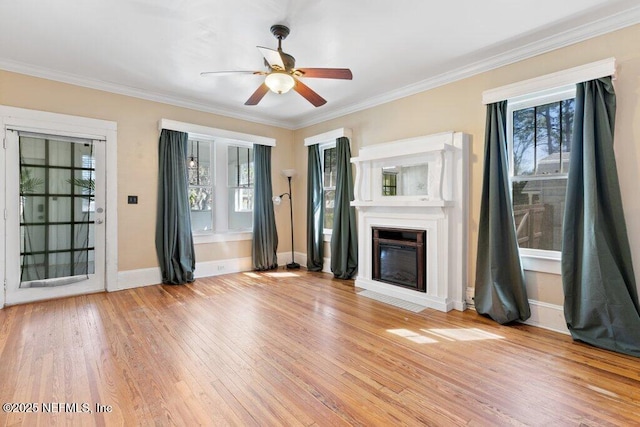 unfurnished living room with a ceiling fan, baseboards, ornamental molding, light wood-type flooring, and a glass covered fireplace