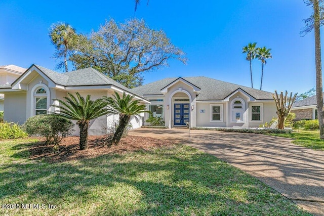 view of front facade with stucco siding, a front lawn, concrete driveway, a shingled roof, and a garage