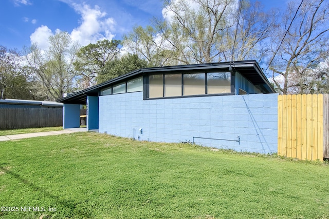 view of side of home with concrete block siding, concrete driveway, a lawn, fence, and an attached carport