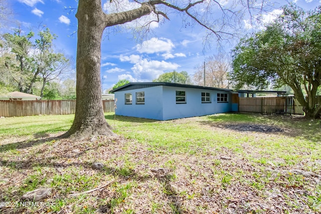 back of house featuring a fenced backyard, a lawn, and stucco siding