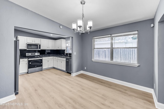 kitchen with white cabinets, dark countertops, vaulted ceiling, stainless steel appliances, and a notable chandelier