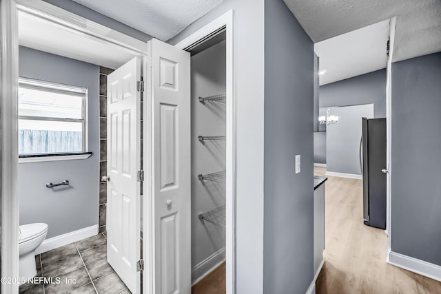 hallway with baseboards, a chandelier, and tile patterned floors