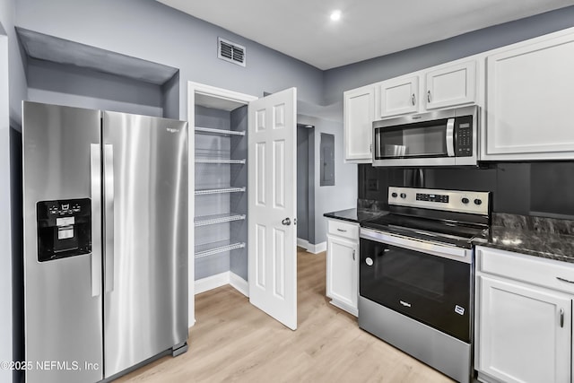 kitchen with visible vents, light wood-style floors, white cabinetry, appliances with stainless steel finishes, and dark stone countertops