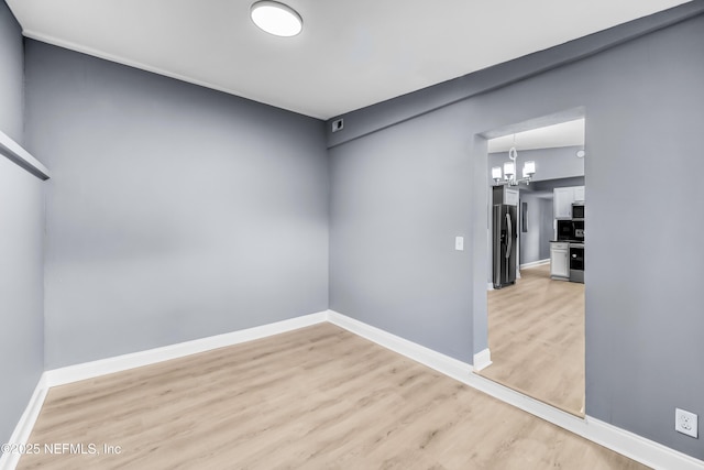 empty room featuring light wood-type flooring, a notable chandelier, and baseboards